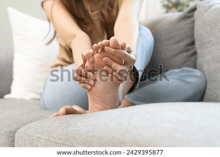 Health care foot pain, suffering asian young woman hand rubbing, massaging sore feet area pain, sitting on sofa at home. Discomfort painful feet ache from walking for long. Physical injury.