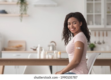 Health care, immunization of population, medical procedure against covid-19 virus. Cheerful young beautiful african american woman show arm with band aid after getting vaccination in kitchen interior