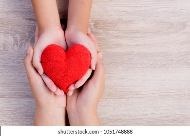 Health Care, Love, Organ Donation, Family Insurance And CSR Concept. Adult And Child Hands Holding Handmade Red Heart On Wooden Background.