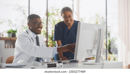 Health Care Medical Hospital. Happy African American Nurse and Black Doctor Having a Casual Conversation, Using Desktop Computer, Laughing and Smiling During a Break at Work - Powered by Shutterstock