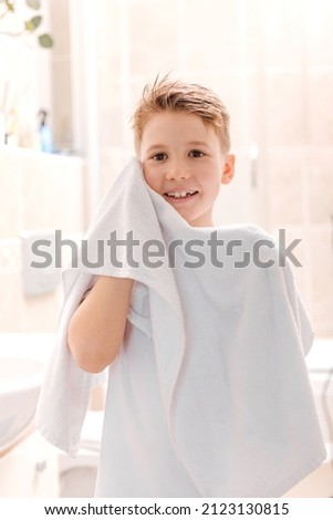 Health care, morning routine, wellness. Cute preteen boy wiping his face with a towel in the bathroom. 