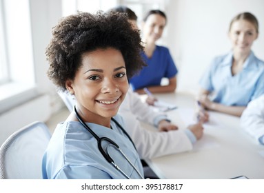 Health Care, Profession, People And Medicine Concept - Happy African American Female Doctor Or Nurse Over Group Of Medics Meeting At Hospital