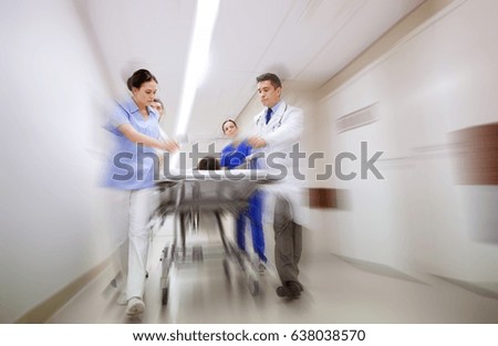 health care, reanimation and medicine concept - group of medics or doctors carrying unconscious woman patient on hospital gurney to emergency (motion blur effect)