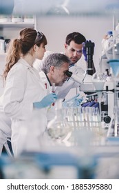 Health Care Researchers Microscoping In Life Science Laboratory. Young Research Scientists And Senior Professor Preparing And Analyzing Microscope Slides In Research Lab.