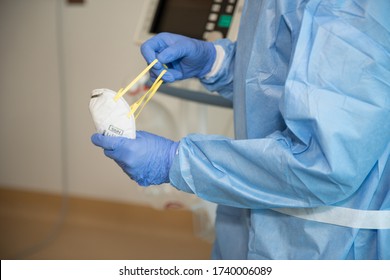 A Health Care Worker Dressed In Gown And Gloves, Prepares And N95 For Putting Over Face