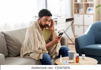 Health, Cold And People Concept - Sick Young Indian Man In Blanket With Smartphone At Home