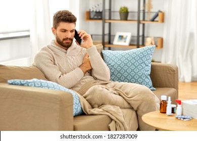 Health, Cold And People Concept - Sick Young Man In Blanket With Smartphone And Medicine Calling Doctor At Home