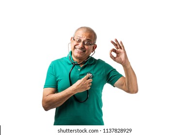 Health Conscious Indian/asian Senior Male Adult Checking Heart Beats With Stethoscope, Holding Toy Heart Or Apple In Other Hand, Showing Ok Sign