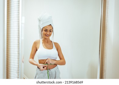 Health conscious woman standing in front of a bathroom mirror. She is pinching an inch from her waist. She is excited to see that her waistline is shrinking due to her current diet plan.