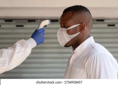 health control staff in virus protection clothing and face shield scanning temperature with digital tool to african american businessman to check for fever in coronavirus covid-19 spreading prevention - Powered by Shutterstock