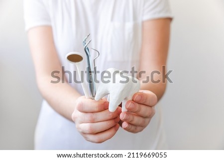 Health dental care concept. Woman hand holding white healthy tooth model and dental dentist tools isolated on white background. Teeth whitening, dental oral hygiene, teeth restoration, dentist day