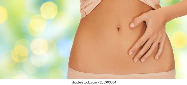 Health, Digestion, Beauty, People And Weigh Loss Concept - Close Up Of Woman Pointing Finger To Belly Over Green Lights Background