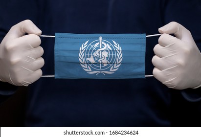Health employee doctor holding medical face mask with WHO (World Health Organization) flag. Coronavirus (COVID-19) pandemic affects the country. 