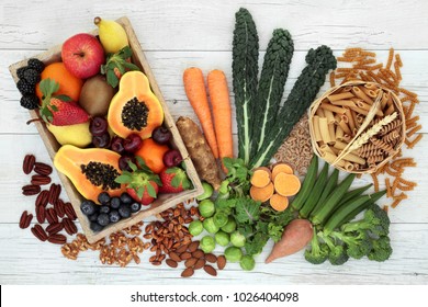 Health food high in fibre with whole wheat pasta, nuts, fruit and vegetables with super foods high in antioxidants, omega 3 fatty acids, anthocyanins and vitamins. Rustic background, top view.