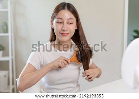 Health hair care, beauty makeup asian woman, girl holding hairbrush and brushing, combing her long straight hair looking at reflection in mirror in morning routine after salon treatment, hairstyle.