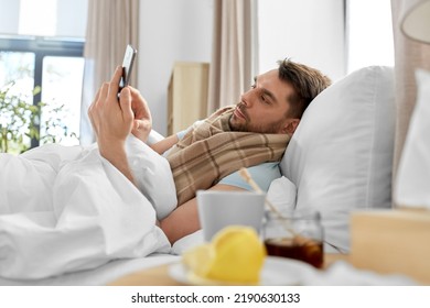 health, illness and people concept - sick man with smartphone in bed at home - Shutterstock ID 2190630133