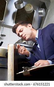 Health Inspector Looking At Oven In Commercial Kitchen