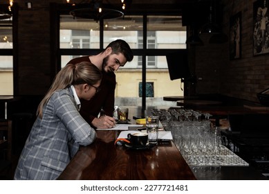 Health inspector sitting in a restaurant and writes a fine and a negative report to the owner or manager of the cafeteria after she finds poor hygiene conditions in the kitchen. Sanitary inspection - Shutterstock ID 2277721481