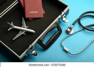 Health Insurance In Travel Concept. Medical Care Abroad. Stethoscope, Toy Airplane And Passports In A Suitcase On A Blue Background