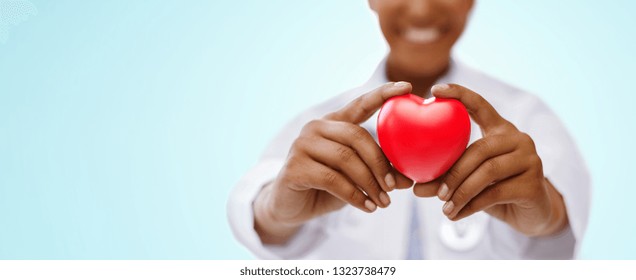 health, medicine and charity concept - close up of african american female doctor hands holding red heart over blue background