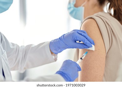 health, medicine and pandemic concept - close up of female doctor or nurse wearing protective medical gloves with syringe vaccinating patient at hospital - Shutterstock ID 1971003029