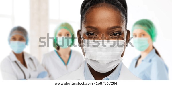 health, medicine and pandemic\
concept - close up of african american female doctor or scientist\
in protective mask over medical workers at hospital on\
background