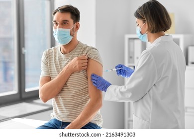 Health, Medicine And Pandemic Concept - Female Doctor Or Nurse Wearing Protective Medical Mask And Gloves With Syringe Vaccinating Male Patient At Hospital