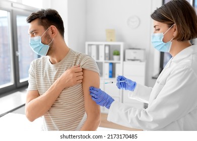 Health, Medicine And Pandemic Concept - Female Doctor Or Nurse Wearing Protective Medical Mask And Gloves With Syringe Vaccinating Male Patient At Hospital