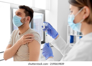 Health, Medicine And Pandemic Concept - Female Doctor Or Nurse Wearing Protective Medical Mask And Gloves With Syringe Vaccinating Male Patient At Hospital