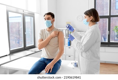 Health, Medicine And Pandemic Concept - Female Doctor Or Nurse Wearing Protective Medical Mask And Gloves With Syringe Vaccinating Male Patient At Hospital