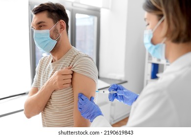 Health, Medicine And Pandemic Concept - Female Doctor Or Nurse Wearing Protective Medical Mask And Gloves With Syringe Vaccinating Male Patient At Hospital