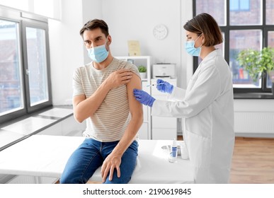 Health, Medicine And Pandemic Concept - Female Doctor Or Nurse Wearing Protective Medical Mask And Gloves With Syringe Vaccinating Male Patient At Hospital