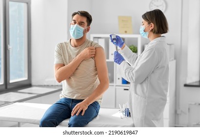 Health, Medicine And Pandemic Concept - Female Doctor Or Nurse Wearing Protective Medical Mask And Gloves With Syringe Vaccinating Male Patient At Hospital