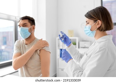 Health, Medicine And Pandemic Concept - Female Doctor Or Nurse Wearing Protective Medical Mask And Gloves With Syringe Vaccinating Male Patient At Hospital