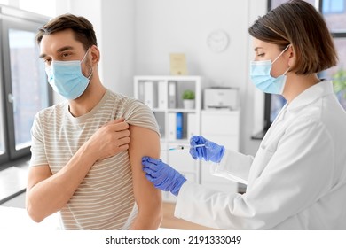 Health, Medicine And Pandemic Concept - Female Doctor Or Nurse Wearing Protective Medical Mask And Gloves With Syringe Vaccinating Male Patient At Hospital