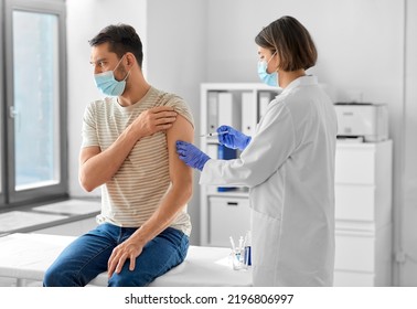 Health, Medicine And Pandemic Concept - Female Doctor Or Nurse Wearing Protective Medical Mask And Gloves With Syringe Vaccinating Male Patient At Hospital