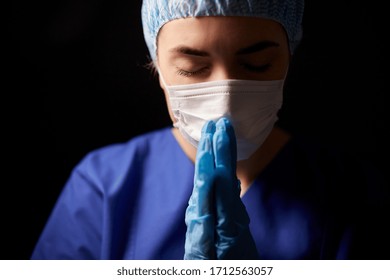 Health, Medicine And Pandemic Concept - Sad Young Female Doctor Or Nurse Wearing Face Protective Mask For Protection From Virus Disease Praying Over Black Background