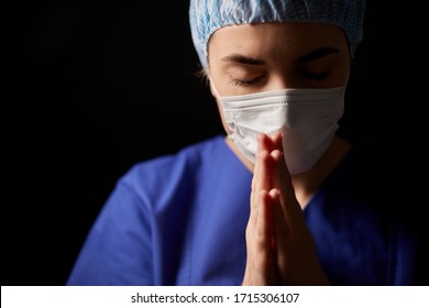 Health, Medicine And Pandemic Concept - Sad Young Female Doctor Or Nurse Wearing Face Protective Mask For Protection From Virus Disease Praying Over Black Background