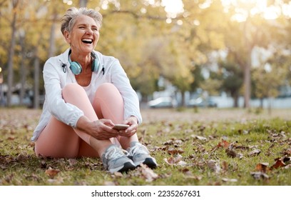 Health, nature and senior woman in park with phone and headphones to relax during fitness workout. Music, happiness and old lady laughing, sitting on ground in garden after running exercise in autumn - Shutterstock ID 2235267631