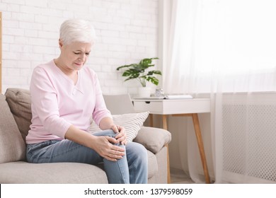 Health problems of old age. Senior woman suffering from pain in leg, massaging her knee at home, empty space