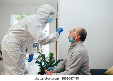 Health Professional in PPE suit and face shield introducing a nasal swab to a senior adult patient at his house. Rapid Antigen Test kit to analyze nasal culture sampling while coronavirus Pandemic.
