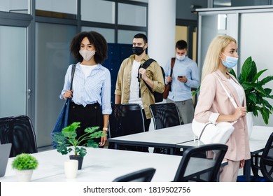 Health Protection And Return To Work After Quarantine Covid-19. Multiracial Young Employees In Protective Masks And With Bags Go To Workplaces In Morning In Modern Office With Green Plants, Copy Space