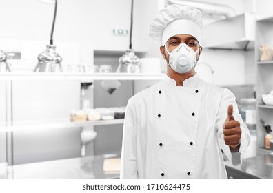 health protection, safety and pandemic concept - indian male chef cook wearing face protective mask or respirator showing thumbs up over restaurant kitchen background - Powered by Shutterstock