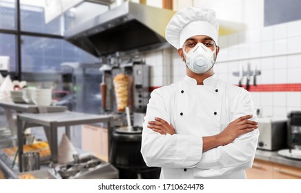 health protection, safety and pandemic concept - indian male chef cook wearing face protective mask or respirator with crossed arms over kebab shop kitchen background - Powered by Shutterstock