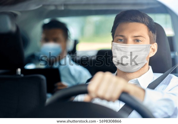 health protection, safety and pandemic concept
- male taxi driver wearing face protective medical mask driving car
with passenger
