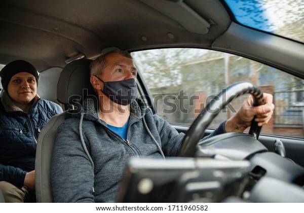 health protection,\
safety and pandemic concept - male taxi driver wearing face\
protective medical mask driving car with passenger. masked taxi\
driver carries a male\
passenger