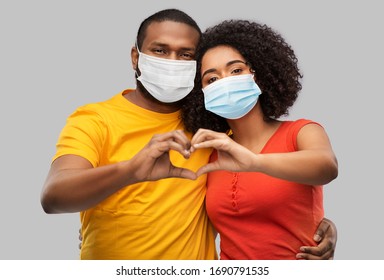health, quarantine and pandemic concept - happy african american couple wearing protective medical masks for protection from virus making hand heart gesture over grey background