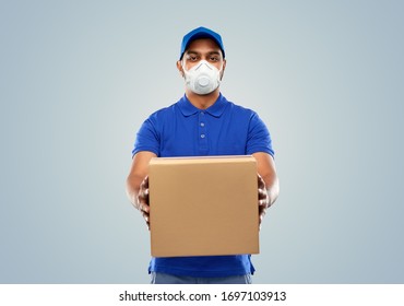health, safety and pandemic concept - happy indian delivery man wearing face protective mask or respirator for protection from virus disease with parcel box in blue uniform over grey background