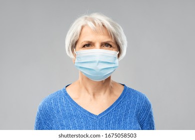 Health, Safety And Pandemic Concept - Portrait Of Senior Woman Wearing Protective Medical Mask For Protection From Virus Over Grey Background