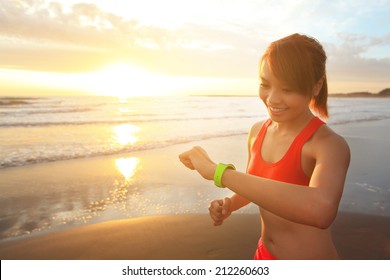 Health Sport Young Woman Run And Look Wear Smart Watch Device With Touchscreen On The Beach At Sunrise, Asian